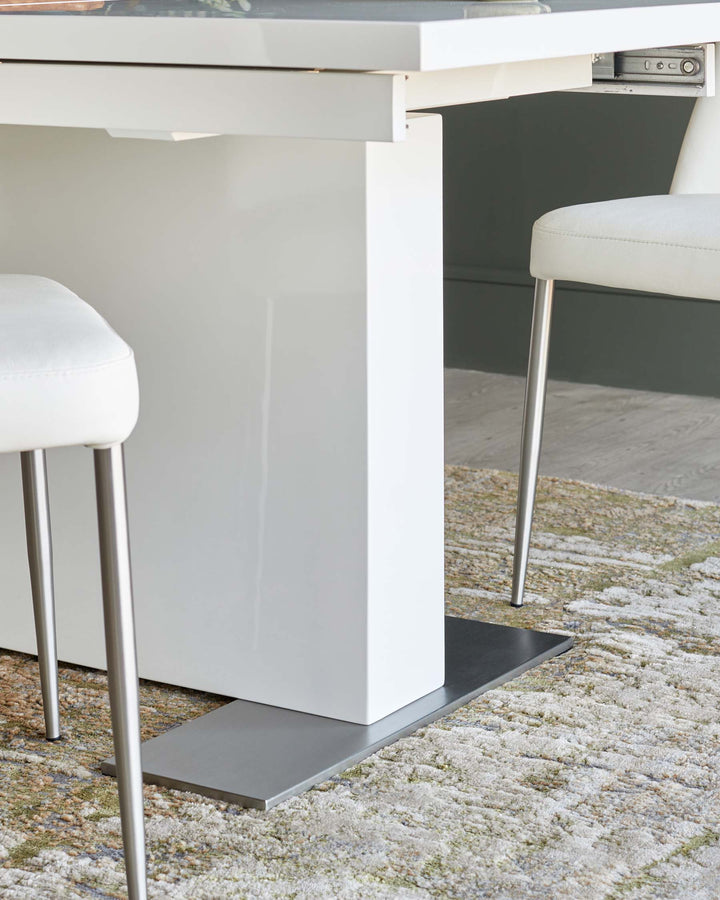 Close-up of a modern white dining table with metal legs, chairs with white leather seats, and a textured rug.