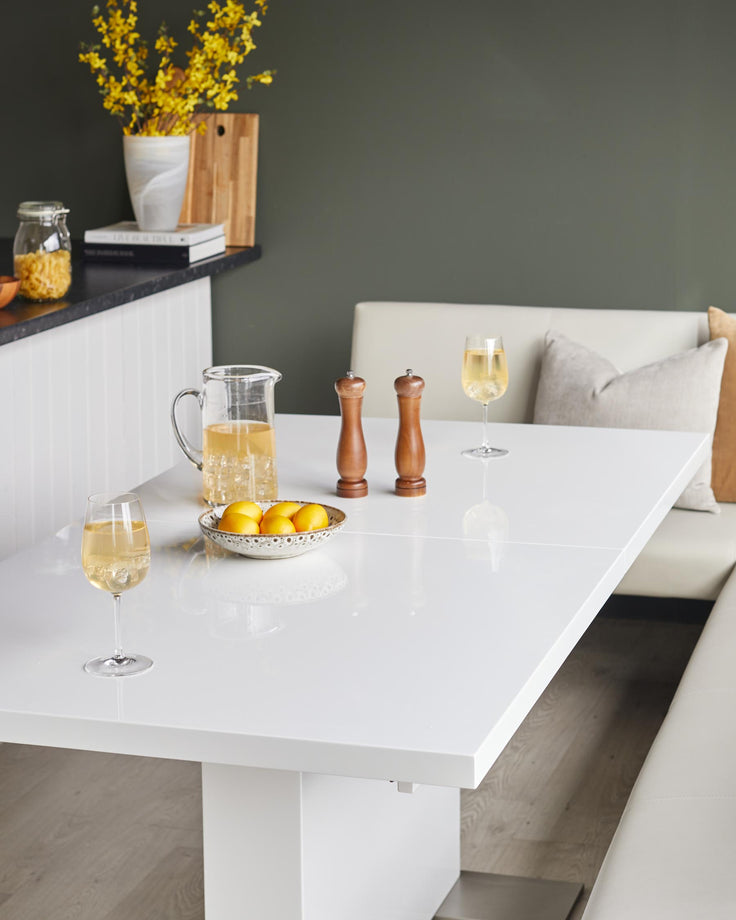 A bright dining space featuring a white table set with drinks, lemons and condiments, plus a built-in bench.