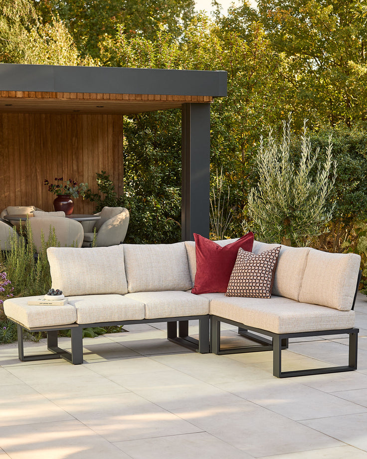 Savannah garden large corner bench with black base, natural cushions, styled in outdoor patio setting with decorative pillows.
