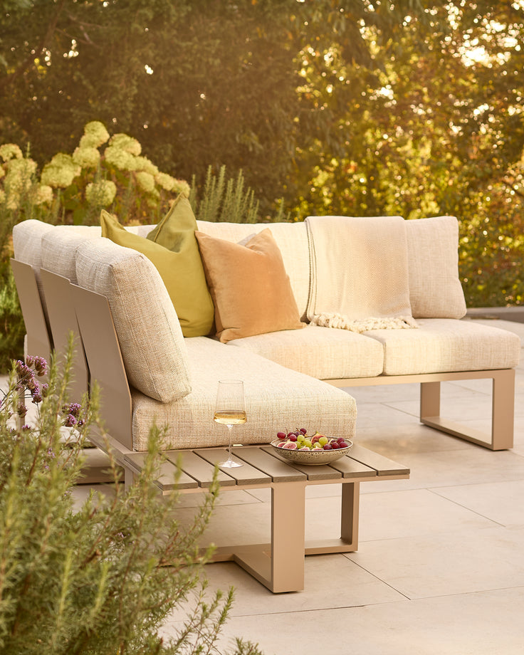 Savannah Garden large corner bench with natural base and cushions, styled with yellow and orange pillows in an outdoor garden setting.