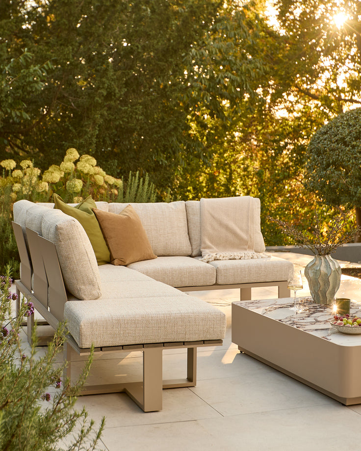 Savannah garden large corner sectional with natural base and beige upholstery, styled with matching coffee table in a lush garden setting.