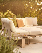 Savannah Garden large corner bench with natural wood base, cream cushions, decorative pillows, and matching coffee table in garden setting.