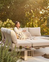 Savannah large corner garden bench with natural base and integrated coffee table, cream cushions, in outdoor setting.