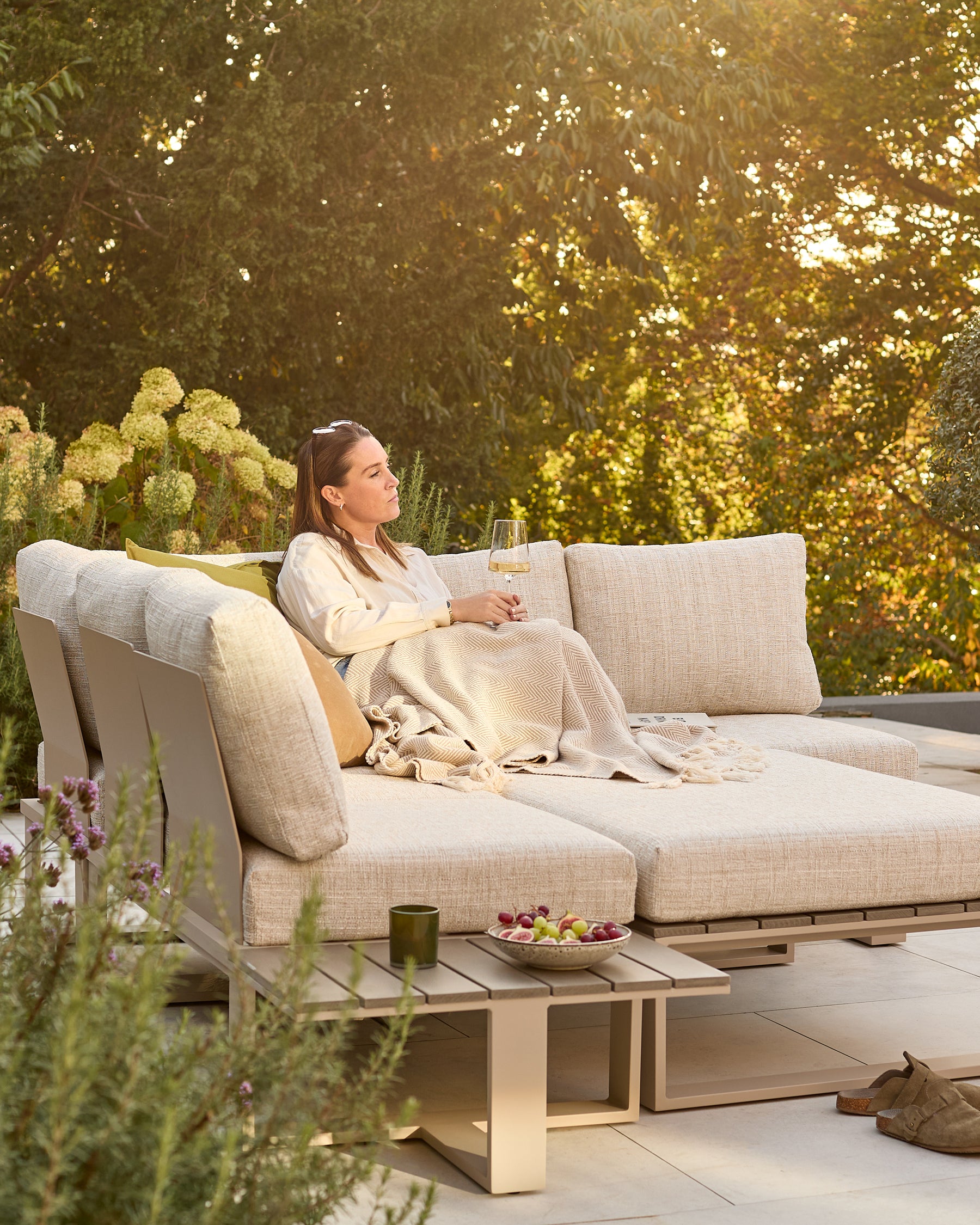 Savannah large corner garden bench with natural base and integrated coffee table, cream cushions, in outdoor setting.