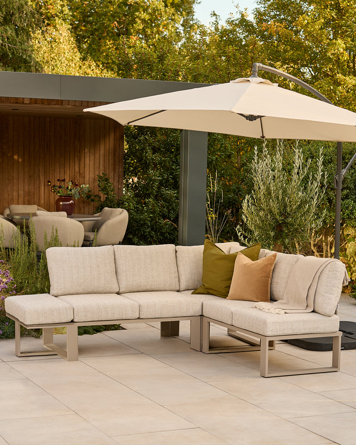Savannah large corner garden bench with natural base, beige cushions, styled under cream umbrella in outdoor patio setting.