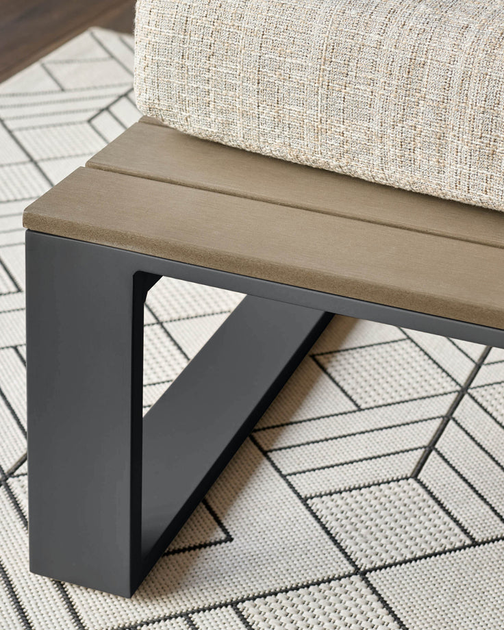 Black metal bench with natural wood seat and cream cushion, shown from side angle on geometric patterned rug.