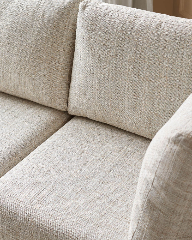Beige linen upholstered corner sofa with cushioned seat and back pillows, close-up detail view.