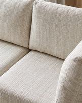 Beige upholstered corner sofa close-up showing textured linen fabric, cushions, and seating detail.