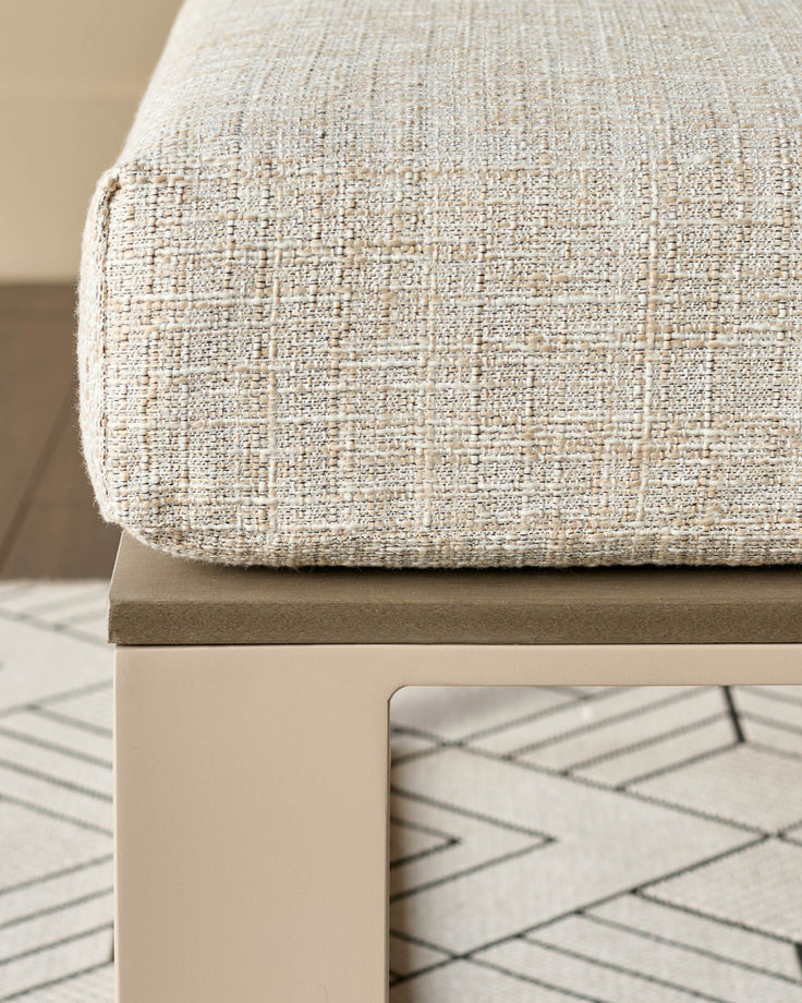 Natural linen bench with textured fabric seat, wooden base, and geometric patterned rug underneath, angled side view.
