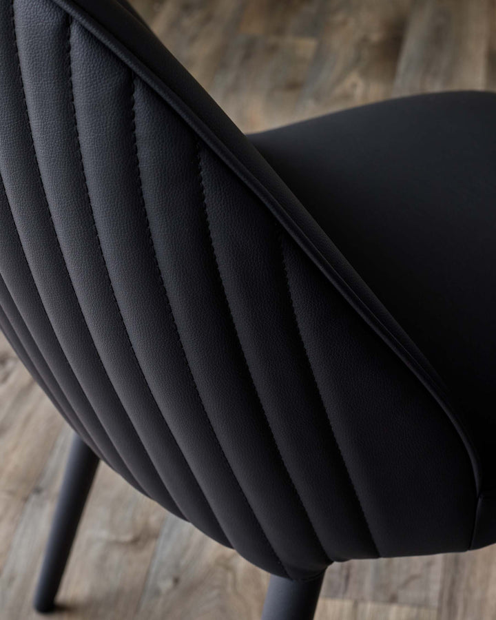 Close-up of a sleek black chair with a quilted backrest, showcasing its modern design and textured upholstery.