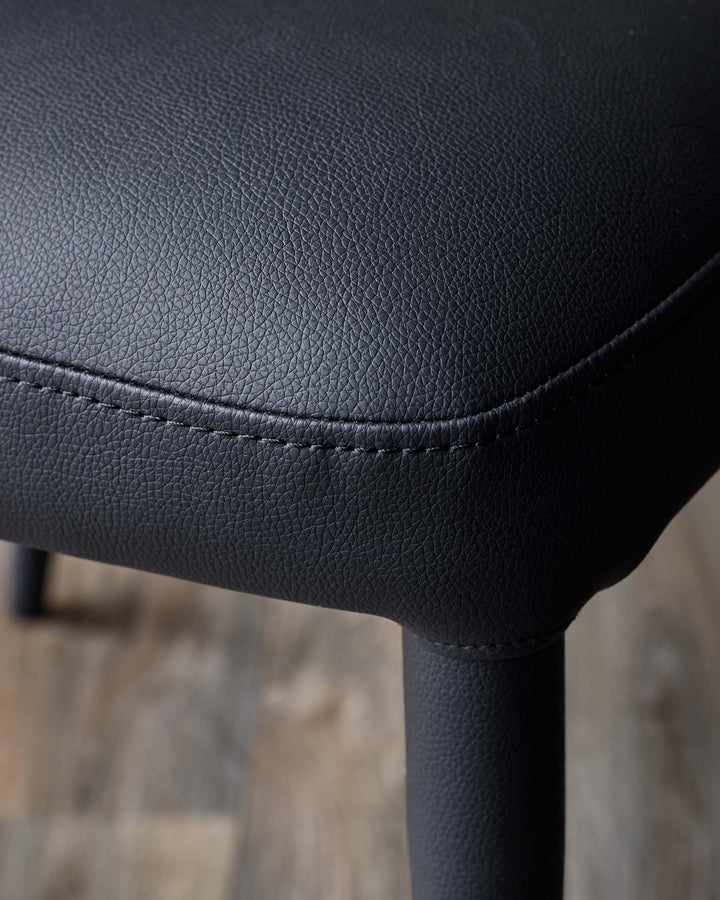 Close-up of a black faux leather seat with detailed stitching, showcasing craftsmanship and material texture.