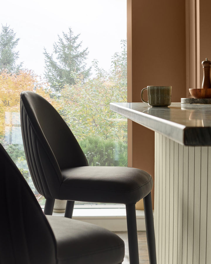 Two stylish bar stools sit at a marble-topped breakfast bar, with a view of autumnal trees through the window.