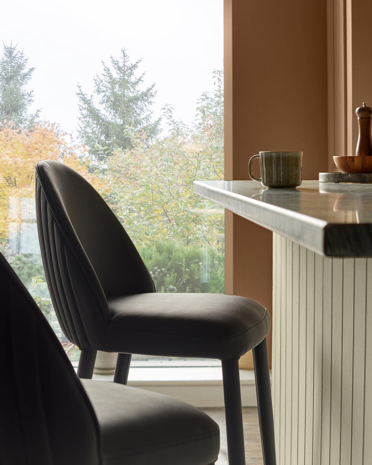 Two stylish bar stools sit at a marble-topped breakfast bar, with a view of autumnal trees through the window.