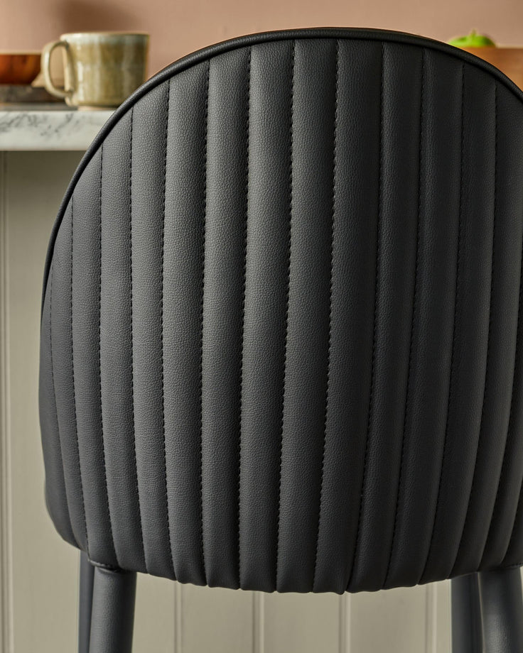 Close-up of a stylish bar stool with a black, vertically-stitched leather back. A modern seating option for kitchen or bar areas.