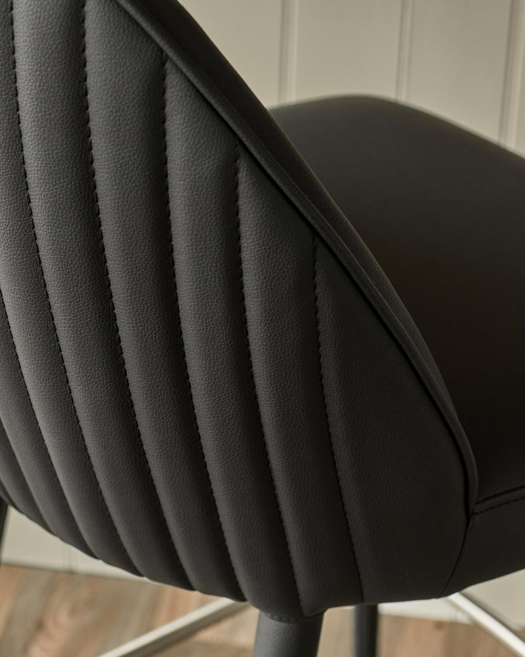 Close-up of a black upholstered bar stool with quilted backrest detail and a smooth seat. Stylish and comfortable seating.