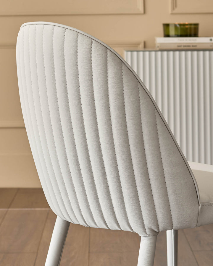 Light grey faux-leather dining chair with vertical stitching detail, shown from back angle in a modern interior setting.