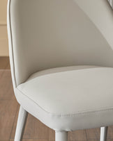 Saylor light grey faux-leather dining chair, side angle view showing curved backrest and stitched seat detail.