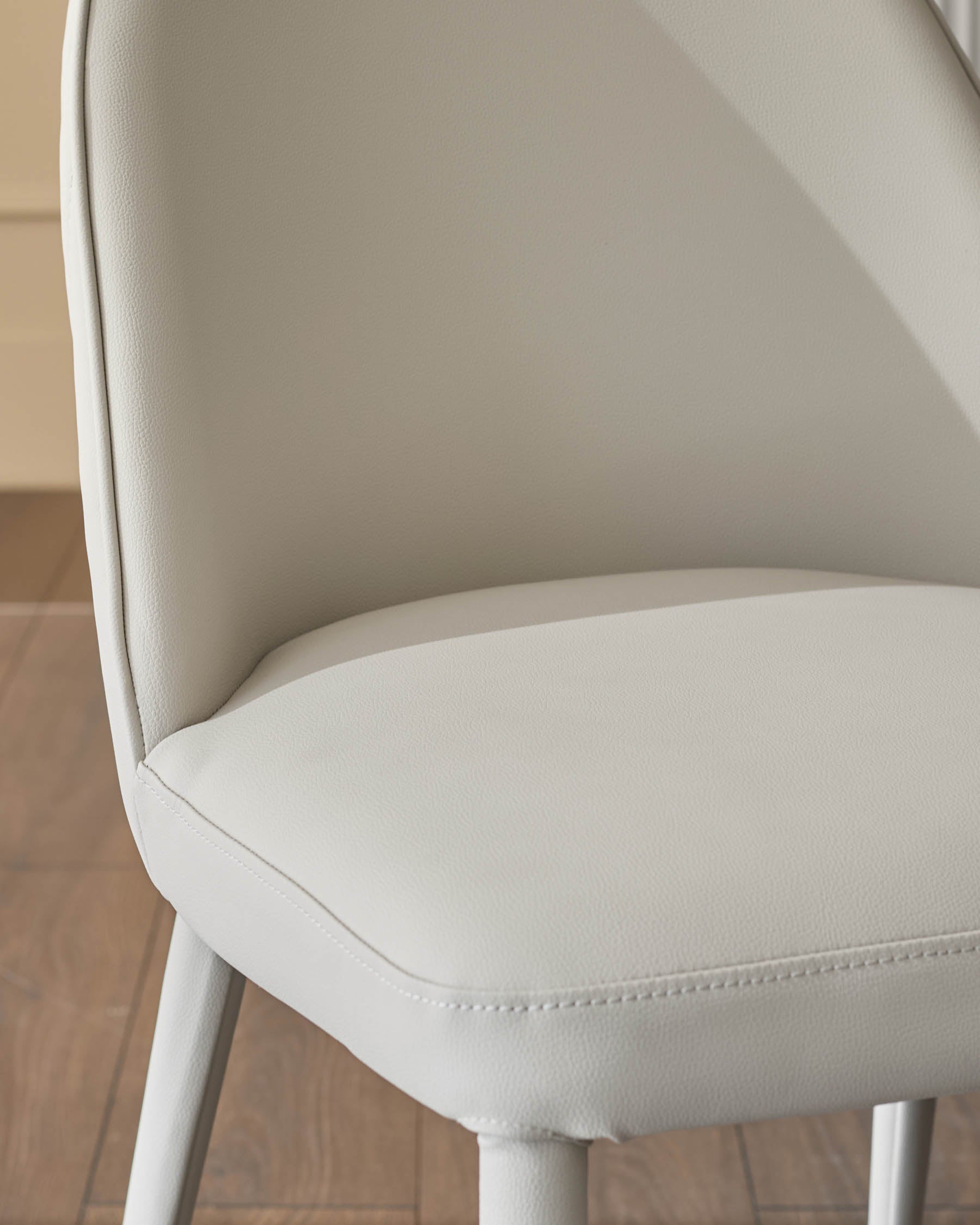 Saylor light grey faux-leather dining chair, side angle view showing curved backrest and stitched seat detail.