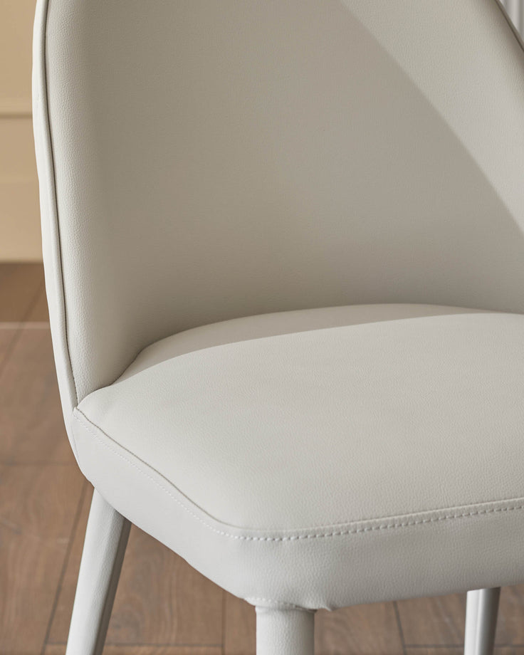 Saylor light grey faux-leather dining chair, side angle view showing curved backrest and stitched seat detail.