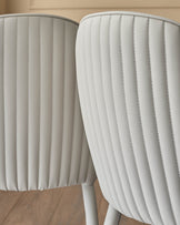 Two light grey faux-leather dining chairs with vertical stitched paneling and curved backrests, shown from a close-up side angle.