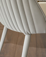 Close-up of light grey faux leather dining chair showing quilted backrest detail and white leg.