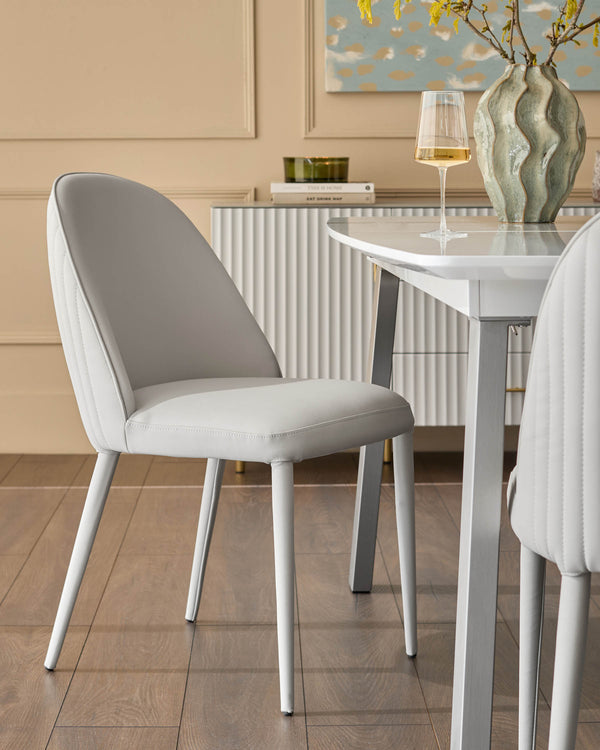 Saylor light grey faux-leather dining chair with curved backrest and white legs, positioned at white table.
