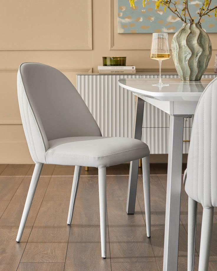 Saylor light grey faux-leather dining chair with curved backrest and white legs, positioned at white table.