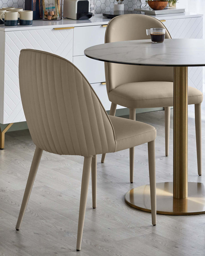 Two upholstered dining chairs around a round marble-topped table with gold base, next to a white sideboard unit.