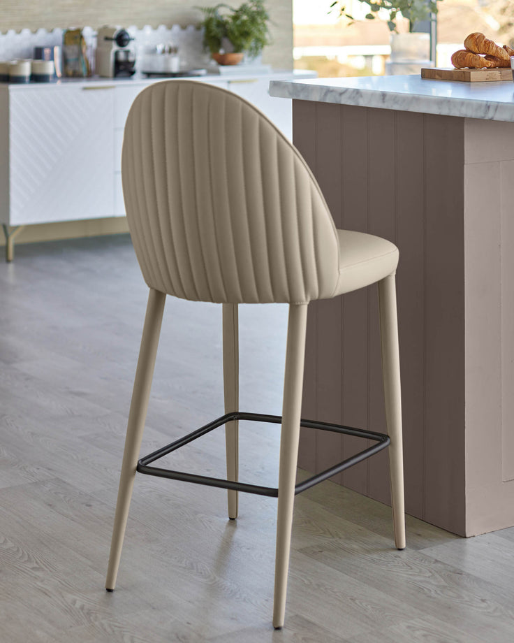 A modern kitchen stool in cream with a black metal footrest, positioned next to a kitchen island.