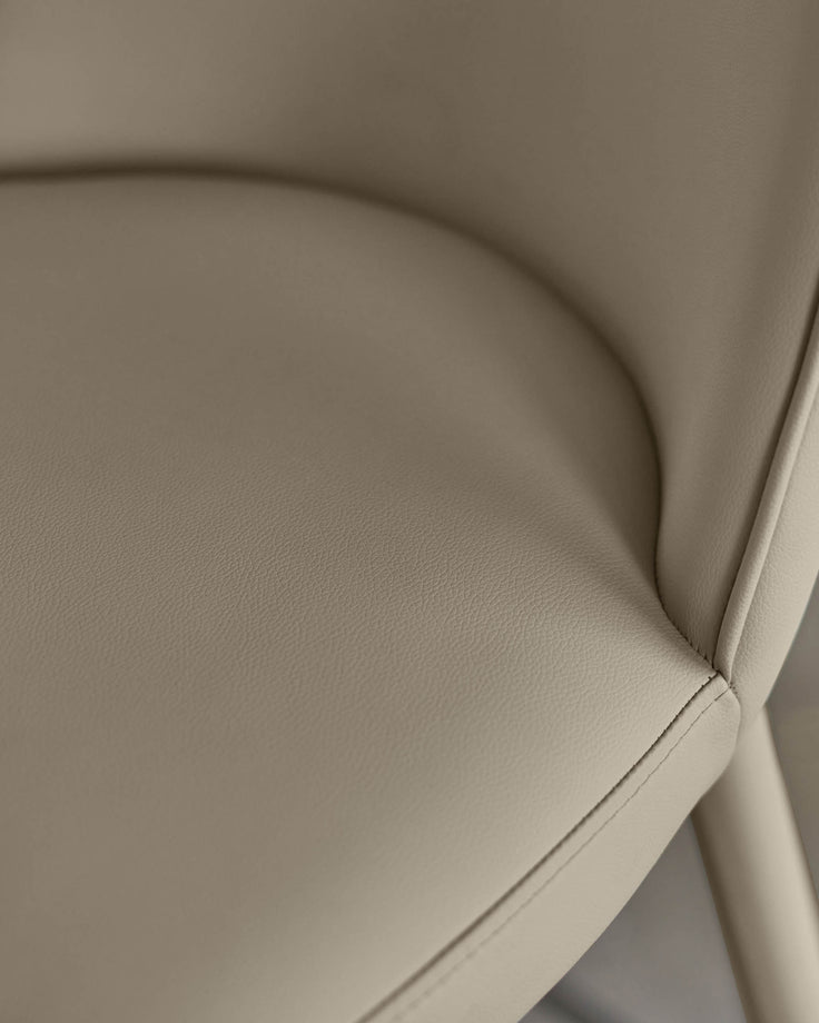Close-up of a stylish, upholstered chair in a neutral, creamy colour. Features sleek lines and detailed stitching.