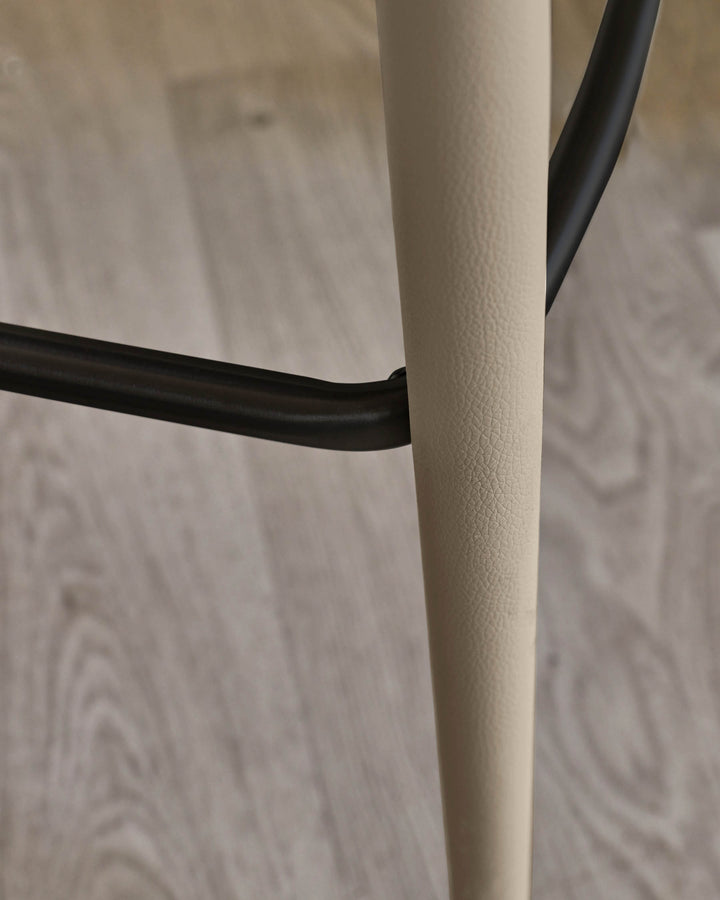 Close-up of a stool with a light cream seat and dark grey metal legs, sat on a light wooden floor.