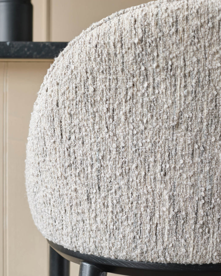 Close-up of a beige boucle chair back showing its texture. The chair has black legs and a black accent piece.