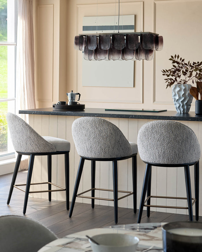Three grey bar stools with dark legs sit at a counter. A modern chandelier hangs above, creating an elegant dining area.