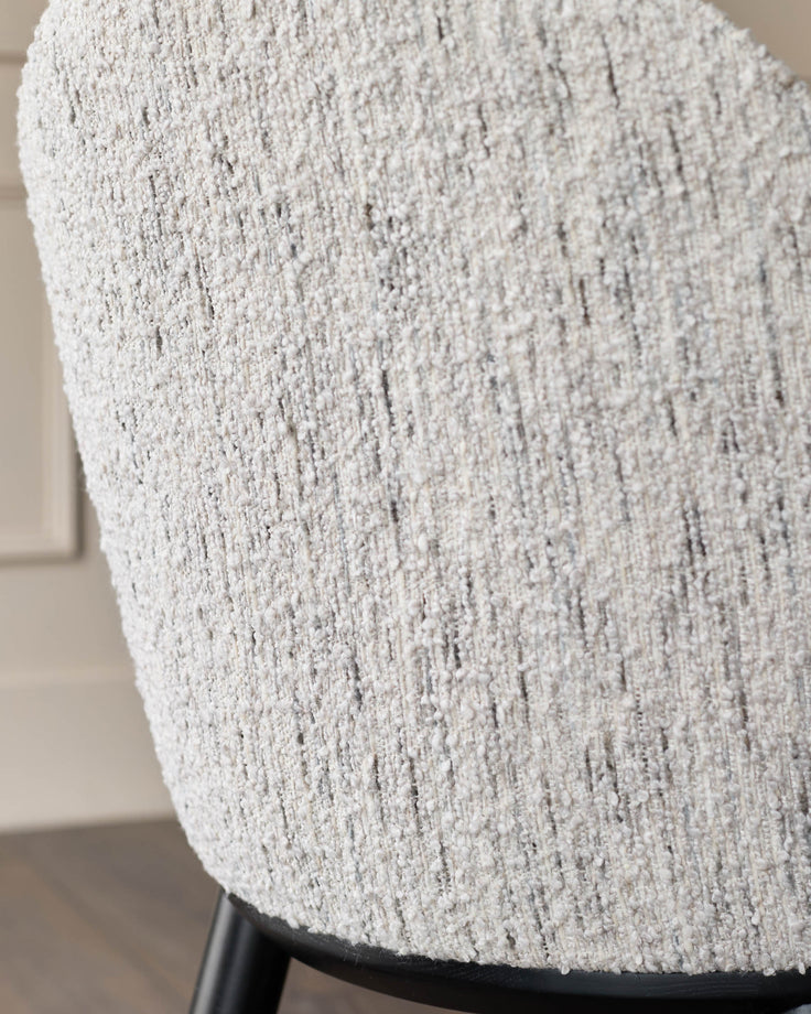Close-up of a textured, neutral-toned chair back with a dark frame. Soft and stylish seating for a contemporary home.