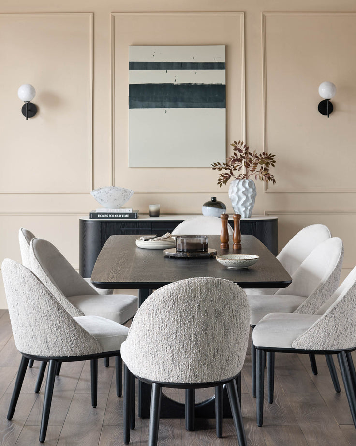 A dining area with a wood table, sideboard and six upholstered chairs, set in front of a beige panelled wall with sconces.