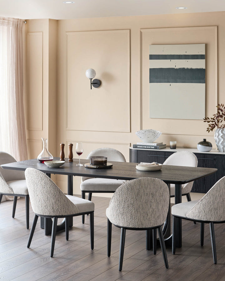 A dining room scene with a dark wood table and six fabric chairs. A sideboard and wall art complete the look.