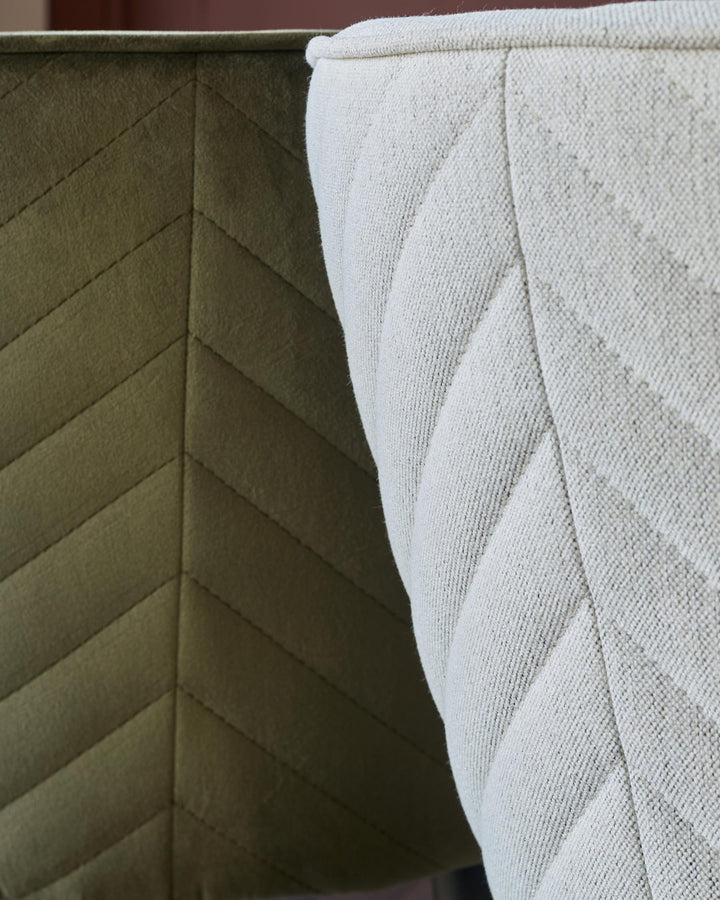 Close up of two upholstered chairs, one olive green and one cream, both with a stitched chevron pattern.