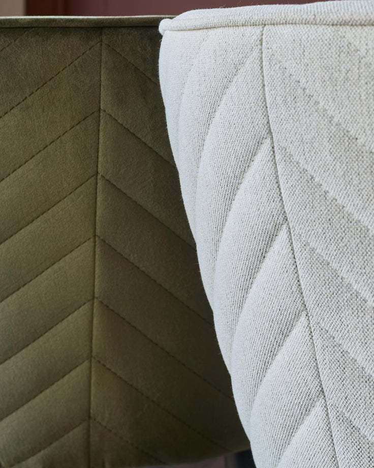 Close up of two upholstered chairs, one olive green and one cream, both with a stitched chevron pattern.