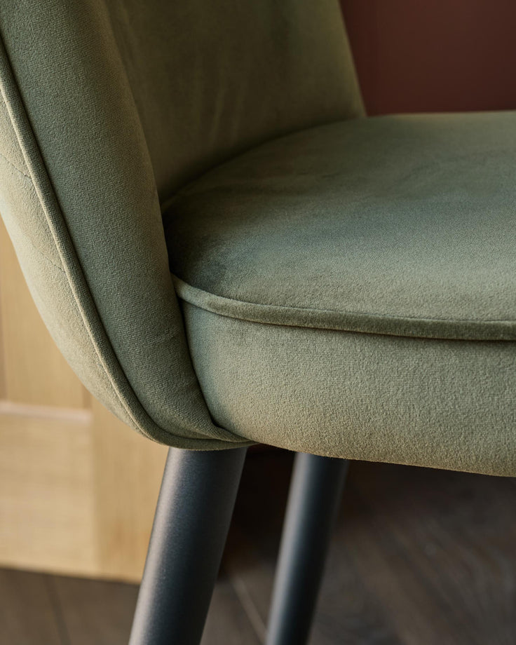 Close up of an upholstered olive green chair with black metal legs.