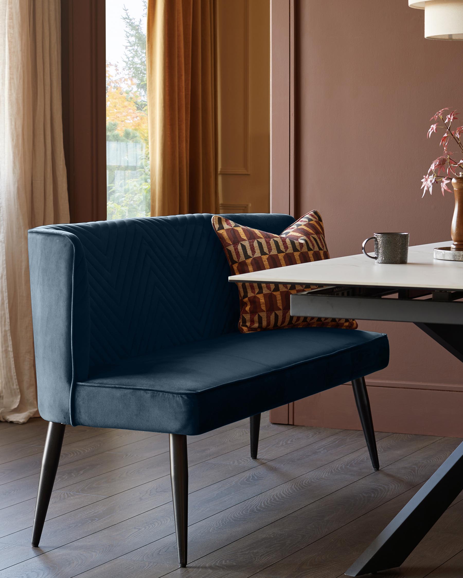 A stylish navy blue velvet bench seat with a geometric cushion, complemented by a modern dining table.
