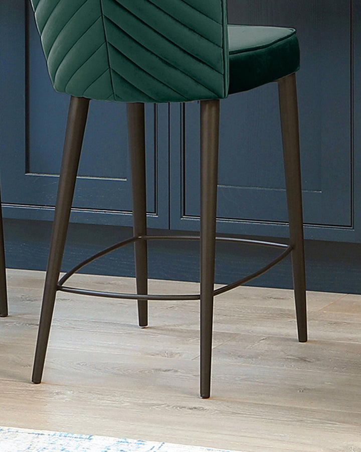Serena velvet bar stool in dark green with angled wooden legs and footrest, shown from side angle.