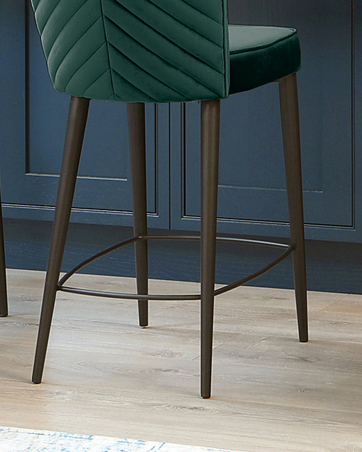 Serena velvet bar stool in dark green with angled wooden legs and footrest, shown from side angle.