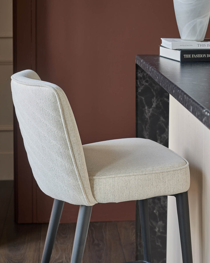 A stylish upholstered bar stool sits next to a kitchen island with a marble countertop.