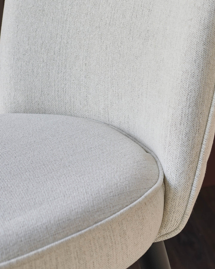 Close-up of a stylish, light-coloured upholstered chair, showcasing its texture and curved design.