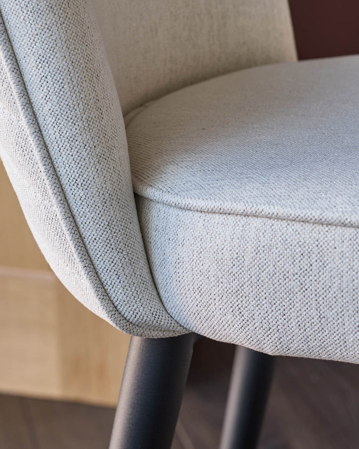 Close-up of a stylish chair with textured light grey fabric and black legs, showcasing comfort and modern design.
