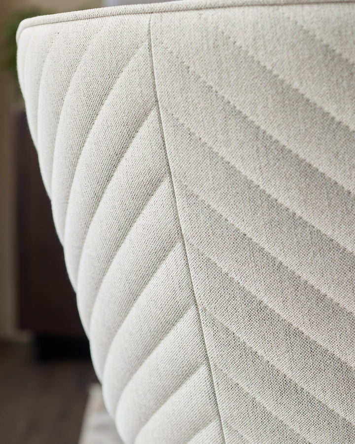 Close-up of a textured, cream-coloured chair with a chevron pattern, showcasing its detailed upholstery and design.