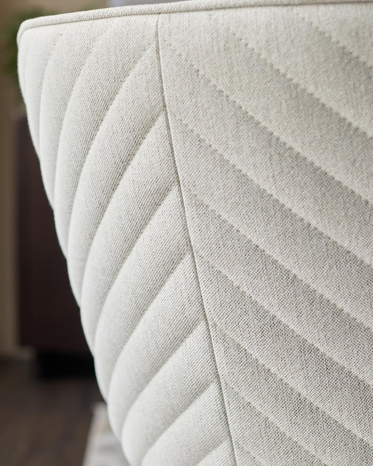Close-up of a textured, cream-coloured chair with a chevron pattern, showcasing its detailed upholstery and design.