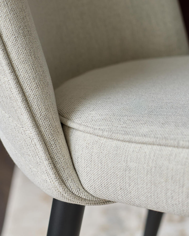 Close-up of a stylish, upholstered chair with a neutral-toned fabric and sleek, dark legs. Ideal for modern living spaces.