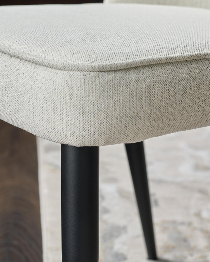 Close-up of a chair with a neutral fabric seat and black metal legs, showcasing its texture and design.