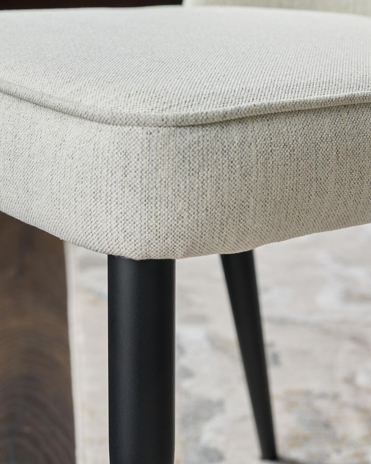 Close-up of a chair with a neutral fabric seat and black metal legs, showcasing its texture and design.